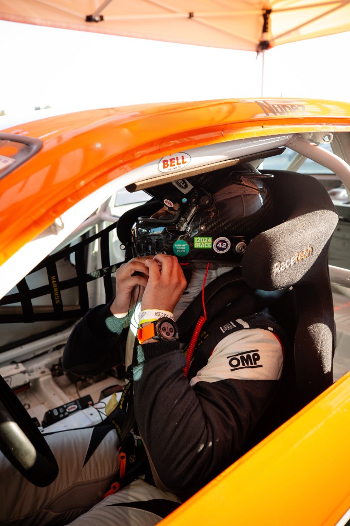 Gianni I. Nunez in a racing helmet and suit, seated in the cockpit of an orange race car